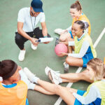 Netball plan, sports team smile and coach planning game strategy, teamwork collaboration or explain competition idea. Coaching athlete, top view or talking group of people listen to fitness challenge